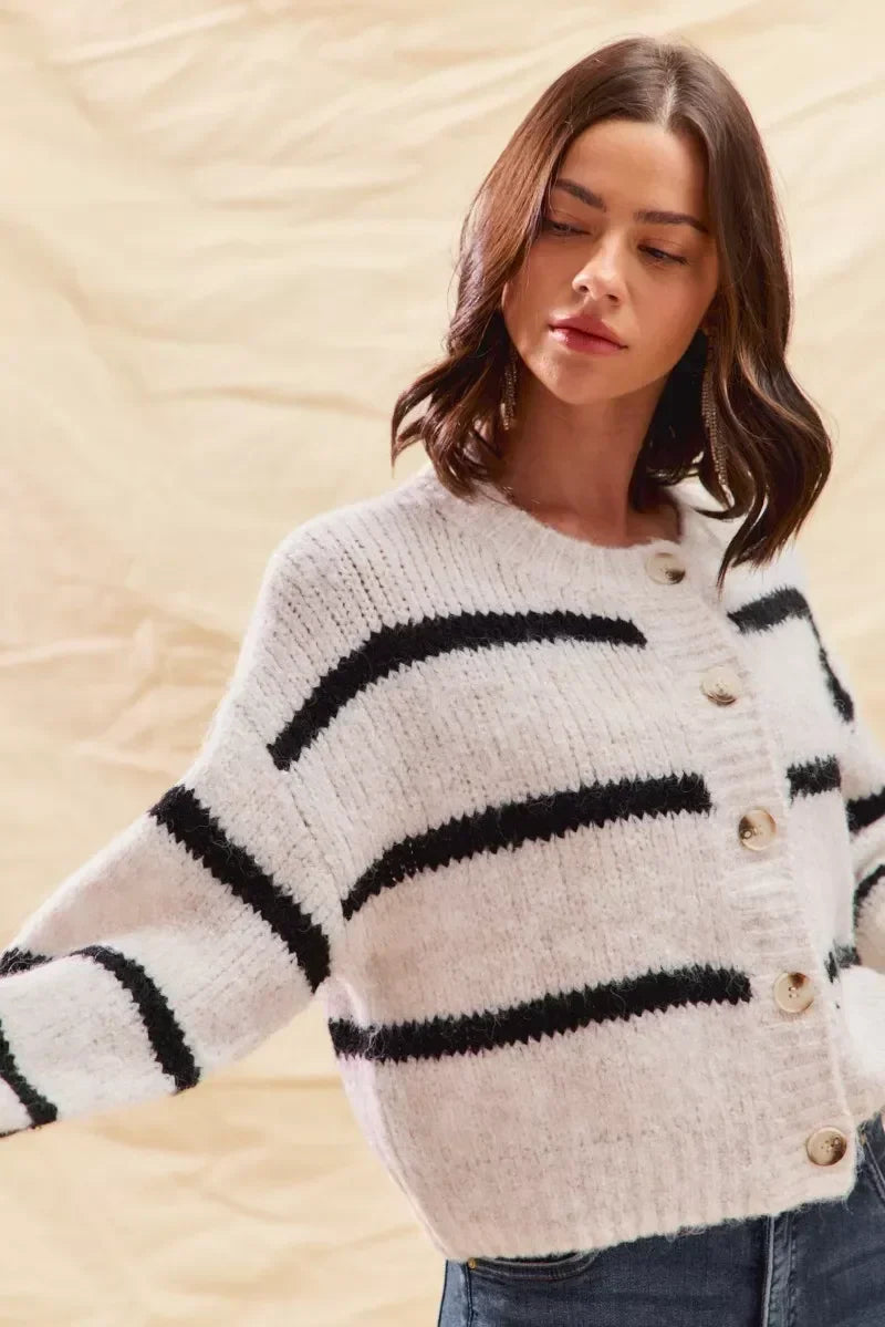 Woman wearing a cozy white cardigan with black stripes and button front, casual style.