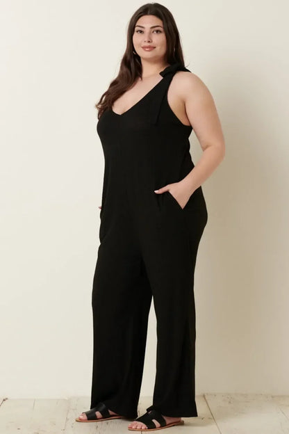 Woman wearing black wide-leg jumpsuit with tie strap shoulders and black sandals