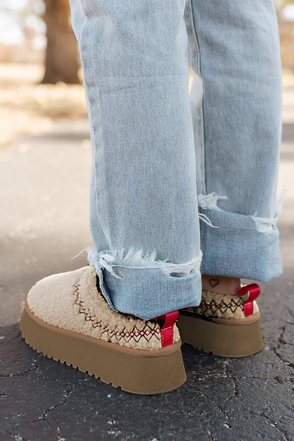 Light wash frayed jeans with shearling platform slip-on shoes and red pull tabs outdoors