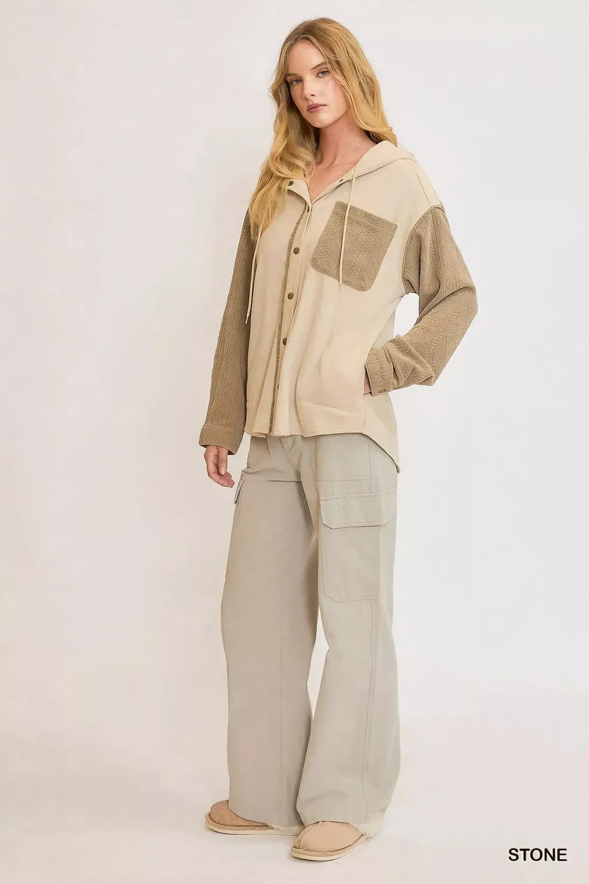 Woman in relaxed stone-colored cargo pants and a button-up hoodie with textured sleeves and pocket.