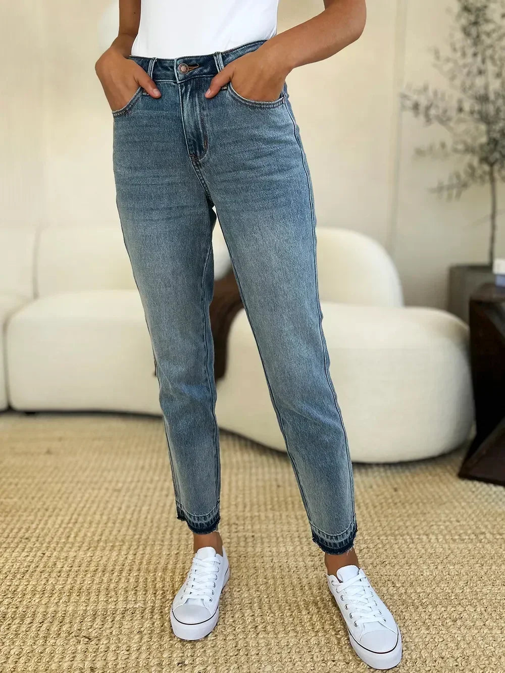 Woman wearing high-waisted, straight-leg blue jeans and white sneakers in a casual setting.