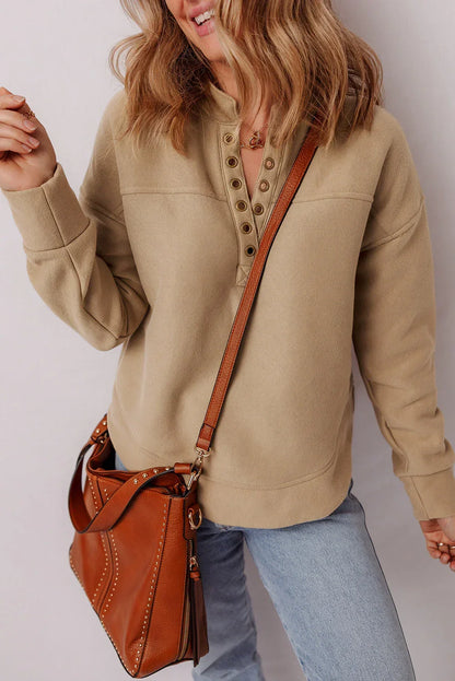 Woman in tan henley pullover, light wash jeans, crossbody brown leather bag