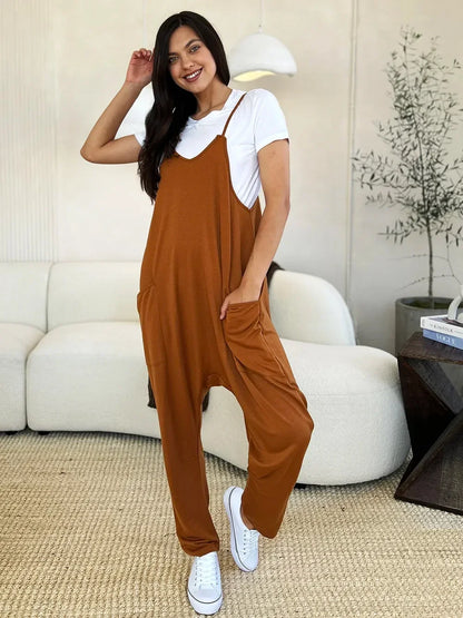 Woman wearing relaxed brown jumpsuit over white t-shirt with white sneakers in modern living room.