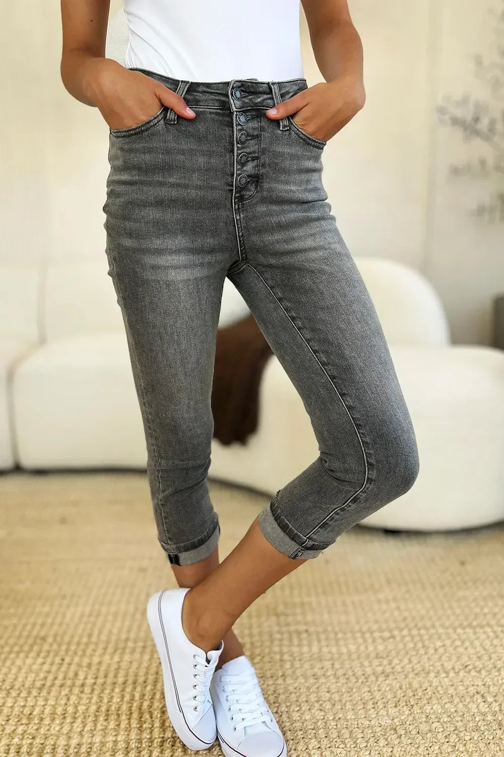 Woman wearing high-waisted grey cropped jeans with rolled cuffs and white sneakers