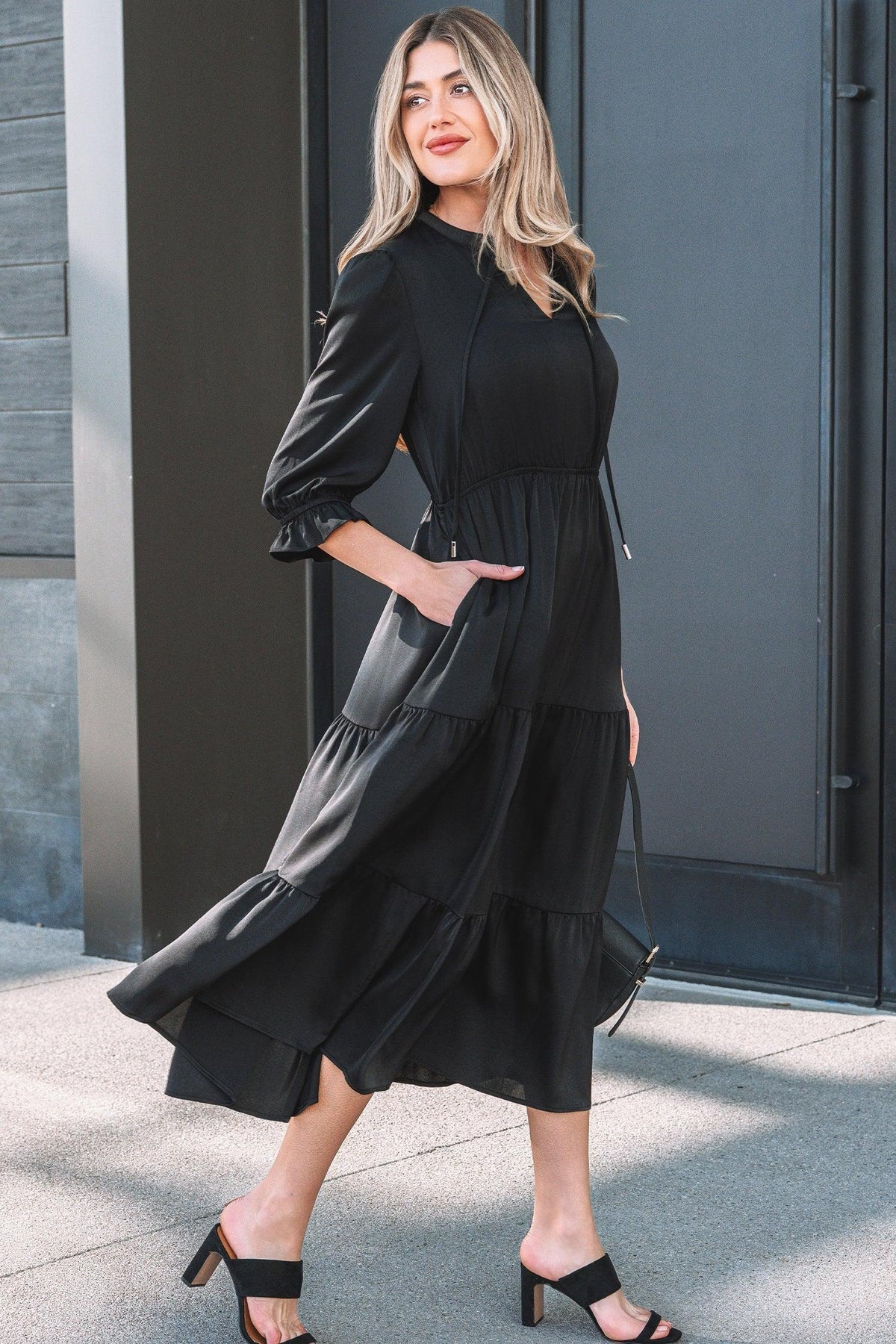 Woman wearing a black tiered midi dress with long sleeves and heeled sandals outdoors