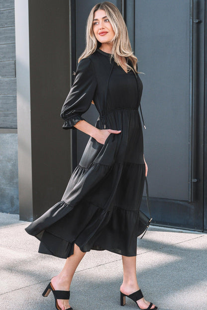 Woman wearing a black tiered midi dress with long sleeves and heeled sandals outdoors