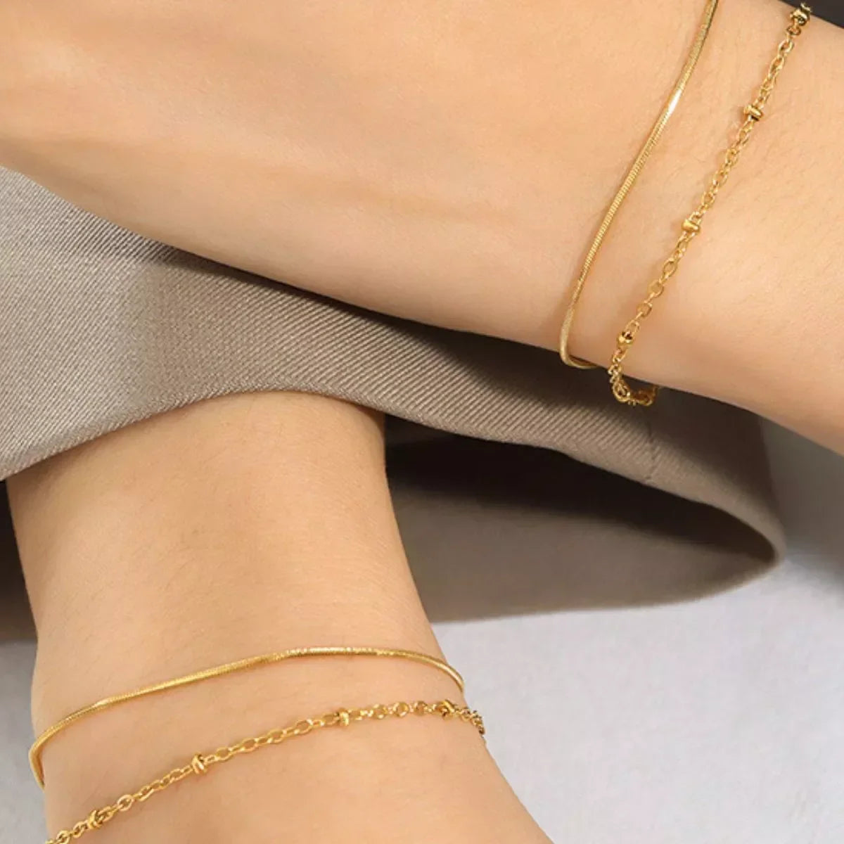 Close-up of minimalist gold chain bracelets worn on a model's wrist and ankle