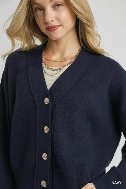 Woman wearing navy blue button-up cardigan with ribbed cuffs and gold chain necklace.