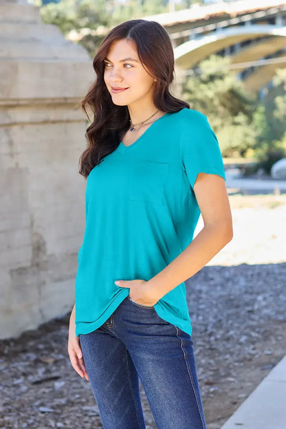 Woman wearing a turquoise V-neck short sleeve top with front pocket and blue jeans outdoors.
