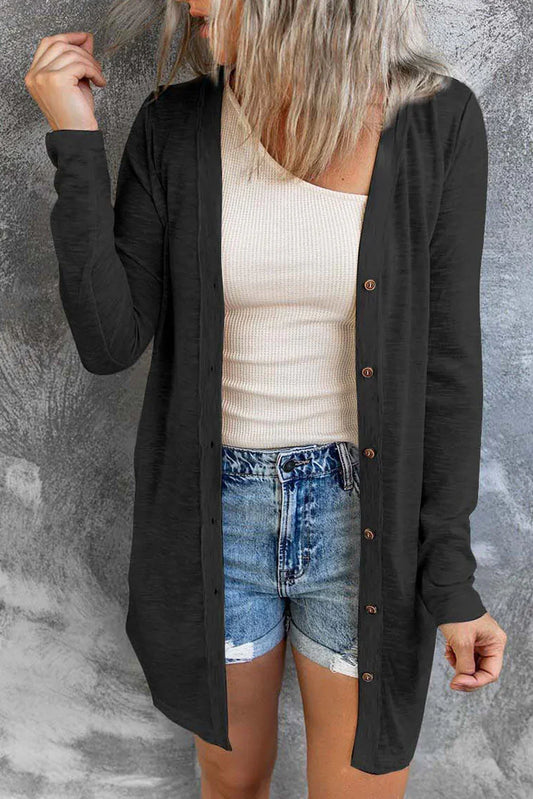 Woman wearing a black button-down cardigan over a beige ribbed tank top and denim shorts
