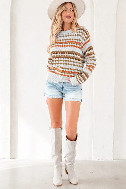 Woman in a patterned knit sweater, denim shorts, knee-high boots and wide-brim hat standing indoors.