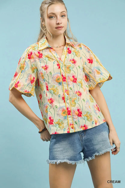 Woman in a floral button-up blouse with short sleeves and denim shorts against a blue background.