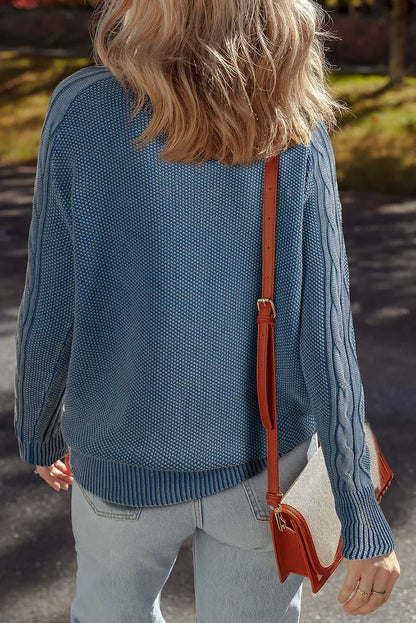 Woman in a blue textured knit sweater with cable sleeves, light jeans, and a crossbody bag