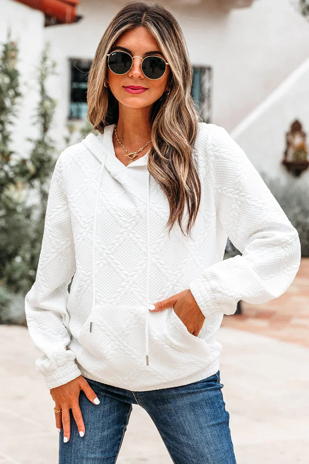 Woman wearing textured white hoodie and blue jeans outdoors, casual modern fashion.