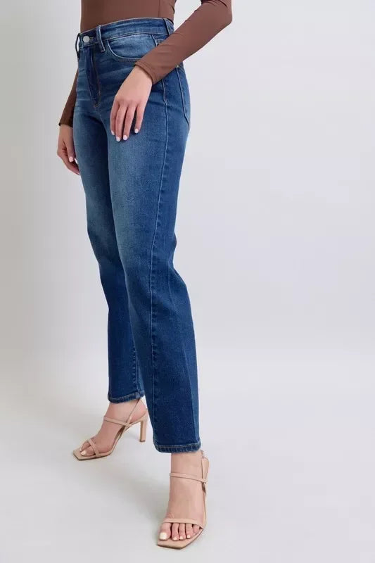 Woman wearing high-waisted straight-leg blue jeans with a brown long-sleeve top and nude heels
