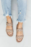 Light wash distressed jeans paired with nude double-strap braided sandals on white tile floor