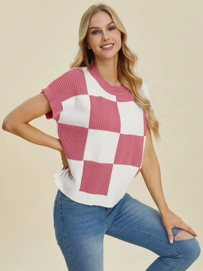 Woman wearing a pink and white checkered knit top with short sleeves and blue jeans.