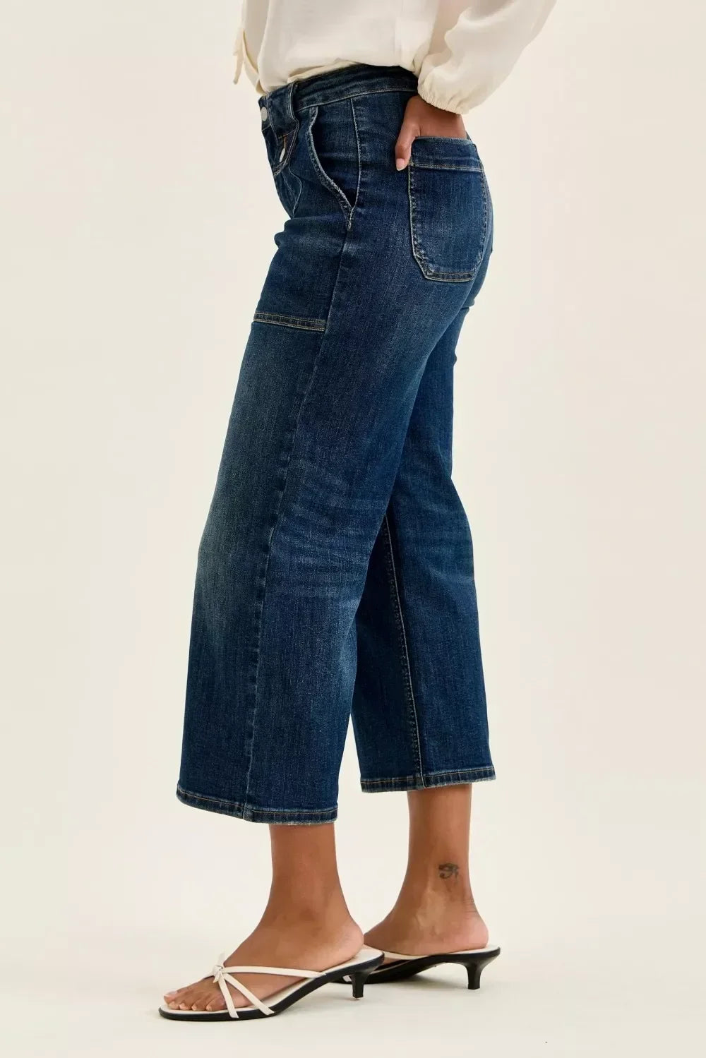 Woman wearing cropped wide leg dark wash jeans with white heeled sandals