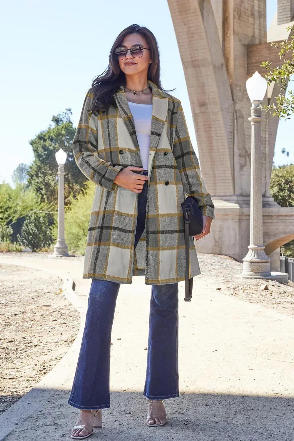 Woman wearing a long plaid coat, white top, blue jeans, and heels outdoors