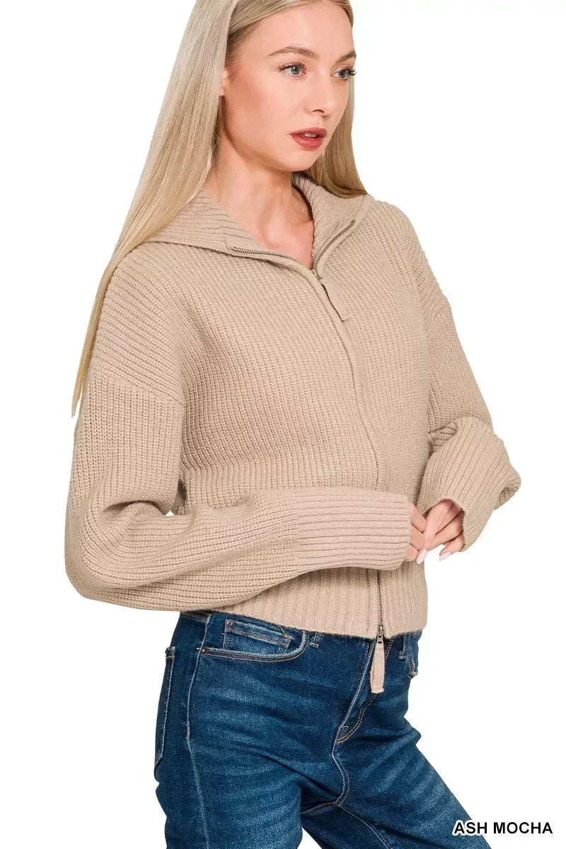 Woman wearing a beige zip-up knit sweater with collar and blue jeans on white background