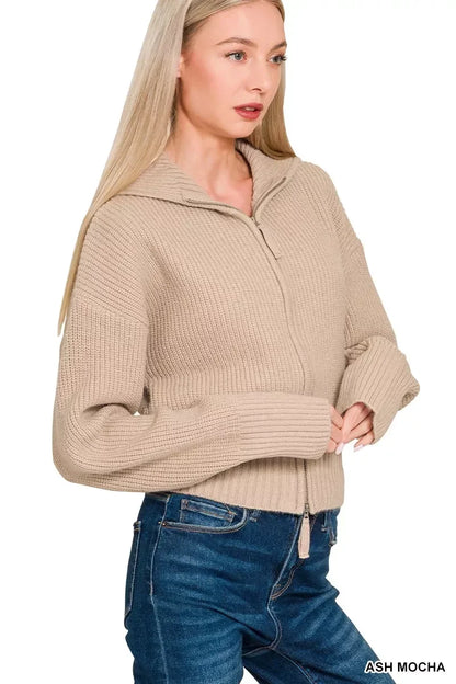 Woman wearing a beige zip-up knit sweater with collar and blue jeans on white background