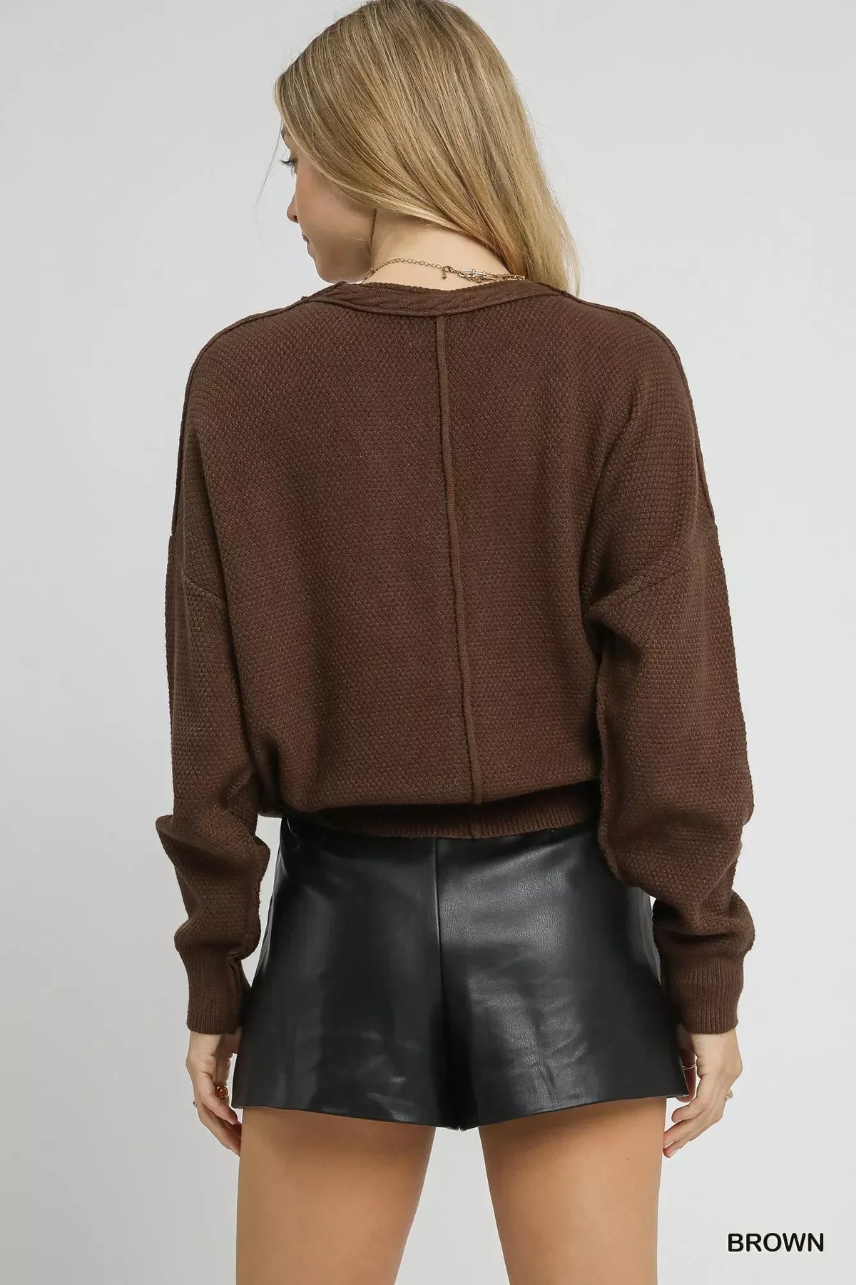 Woman wearing brown knit sweater and black faux leather shorts, shown from the back