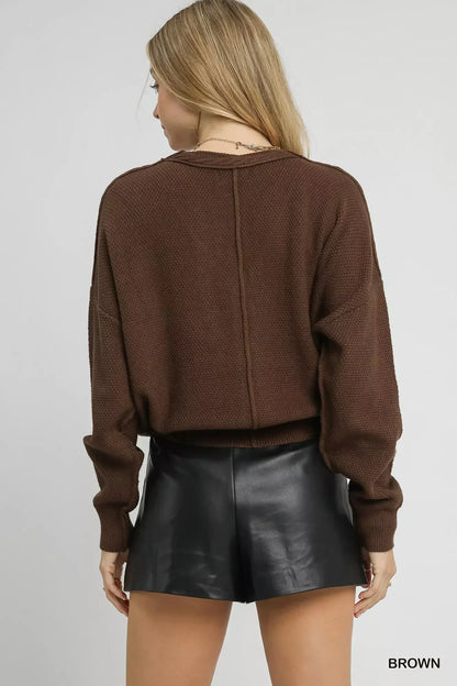 Woman wearing brown knit sweater and black faux leather shorts, shown from the back