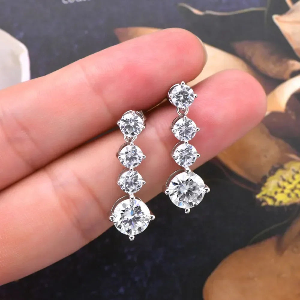 Hand holding silver drop earrings with four round clear gemstones each