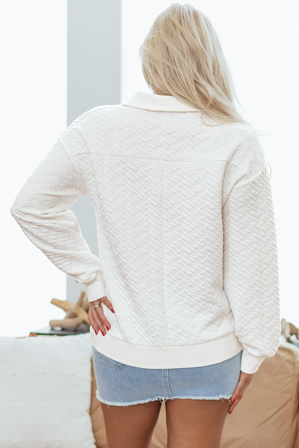 Woman wearing quilted white long sleeve top and light denim shorts indoors
