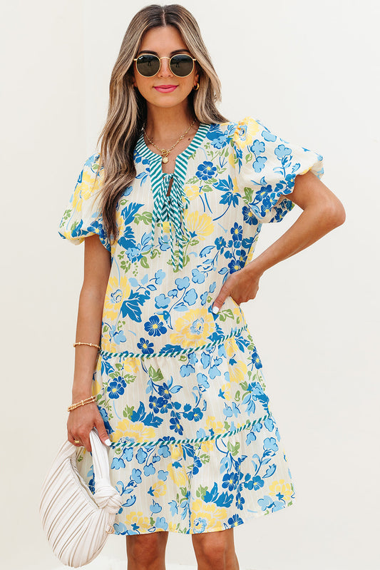 Woman wearing a blue and yellow floral print dress with puff sleeves and a white handbag