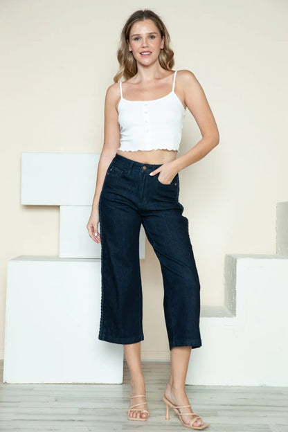 Woman in a white crop top and wide-leg dark denim jeans with strappy heels, standing indoors.