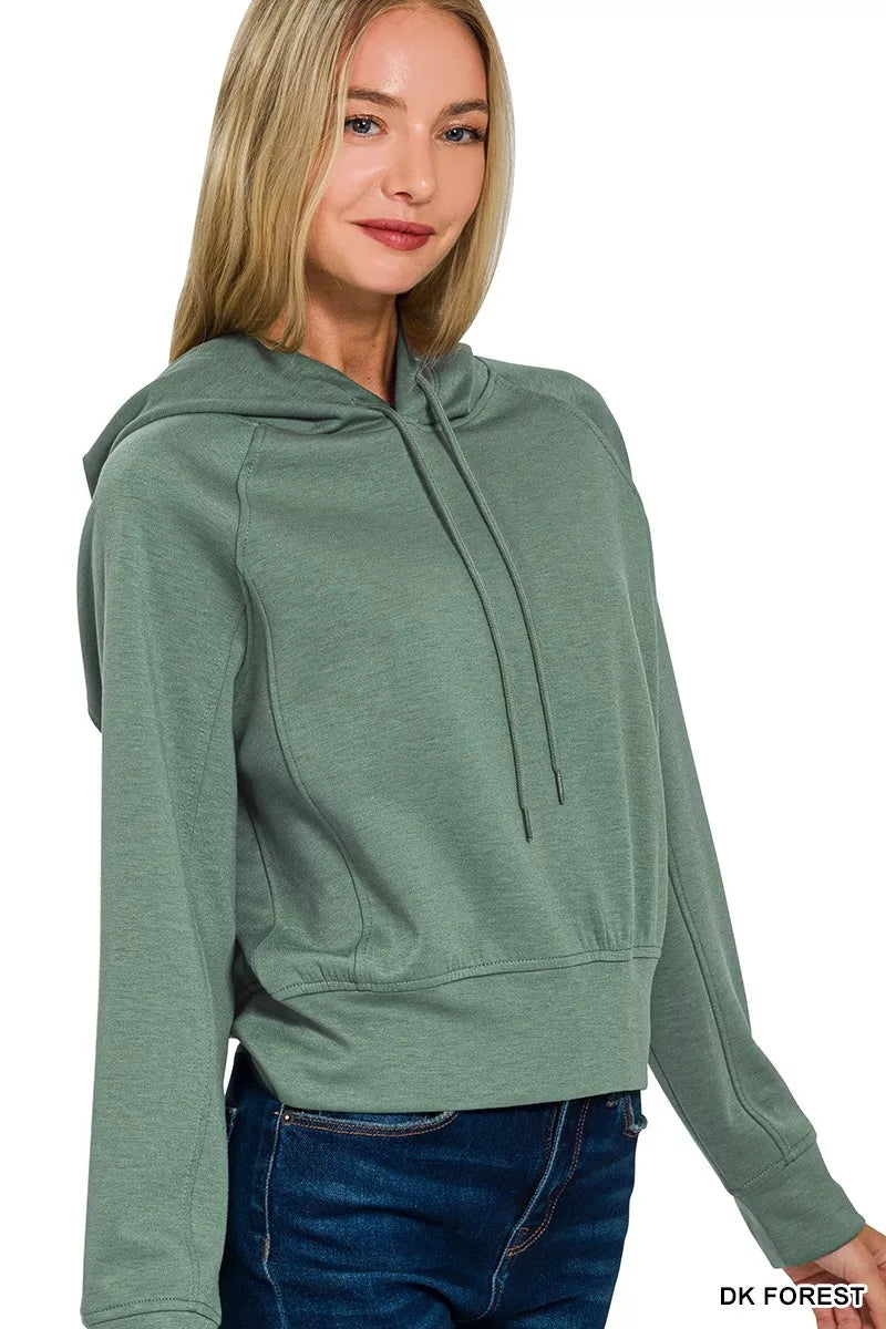 Woman wearing a dark forest green hooded sweatshirt with long sleeves and blue jeans