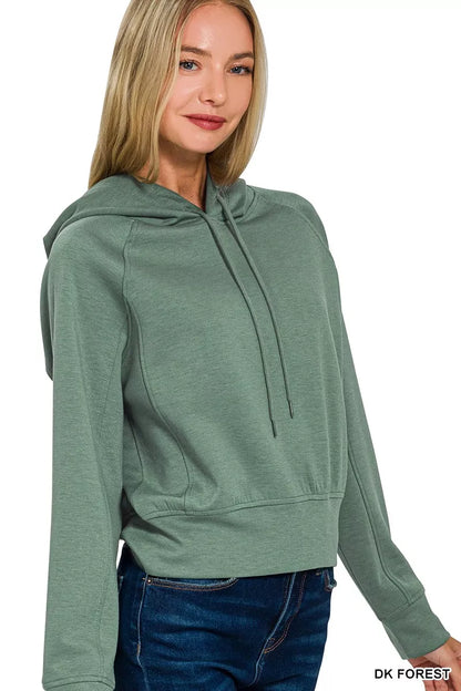 Woman wearing a dark forest green hooded sweatshirt with long sleeves and blue jeans