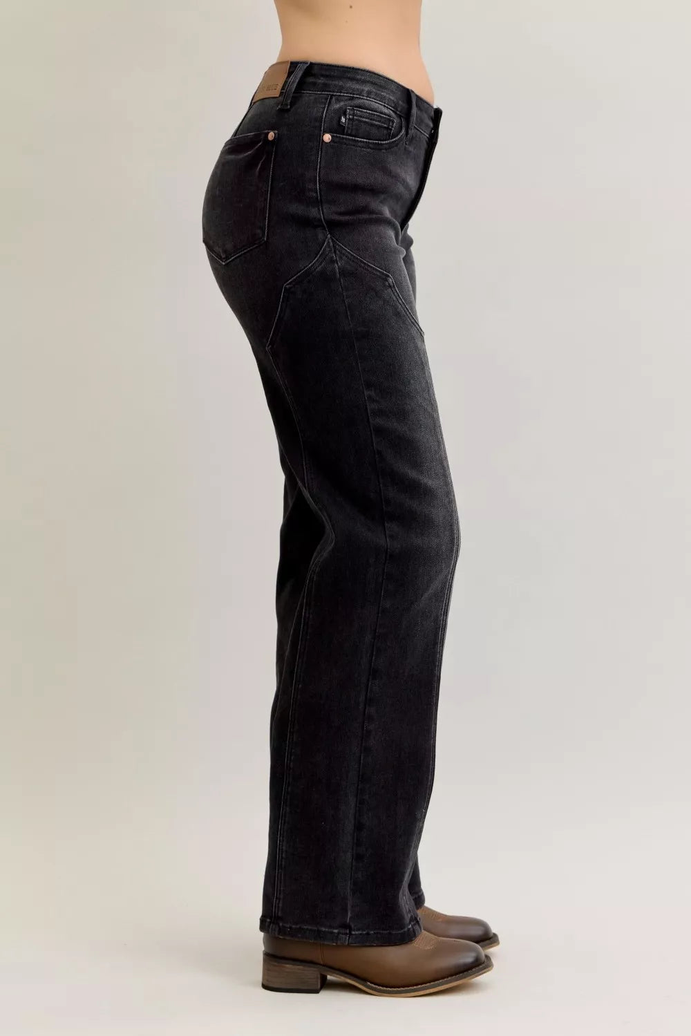 Side view of a woman wearing high-waisted black straight-leg jeans and brown shoes.
