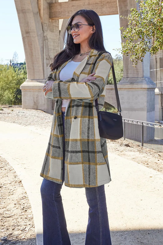 Woman wearing a yellow and gray plaid coat, white top, blue jeans, and sunglasses outdoors