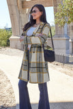 Woman wearing a yellow and gray plaid coat, white top, blue jeans, and sunglasses outdoors