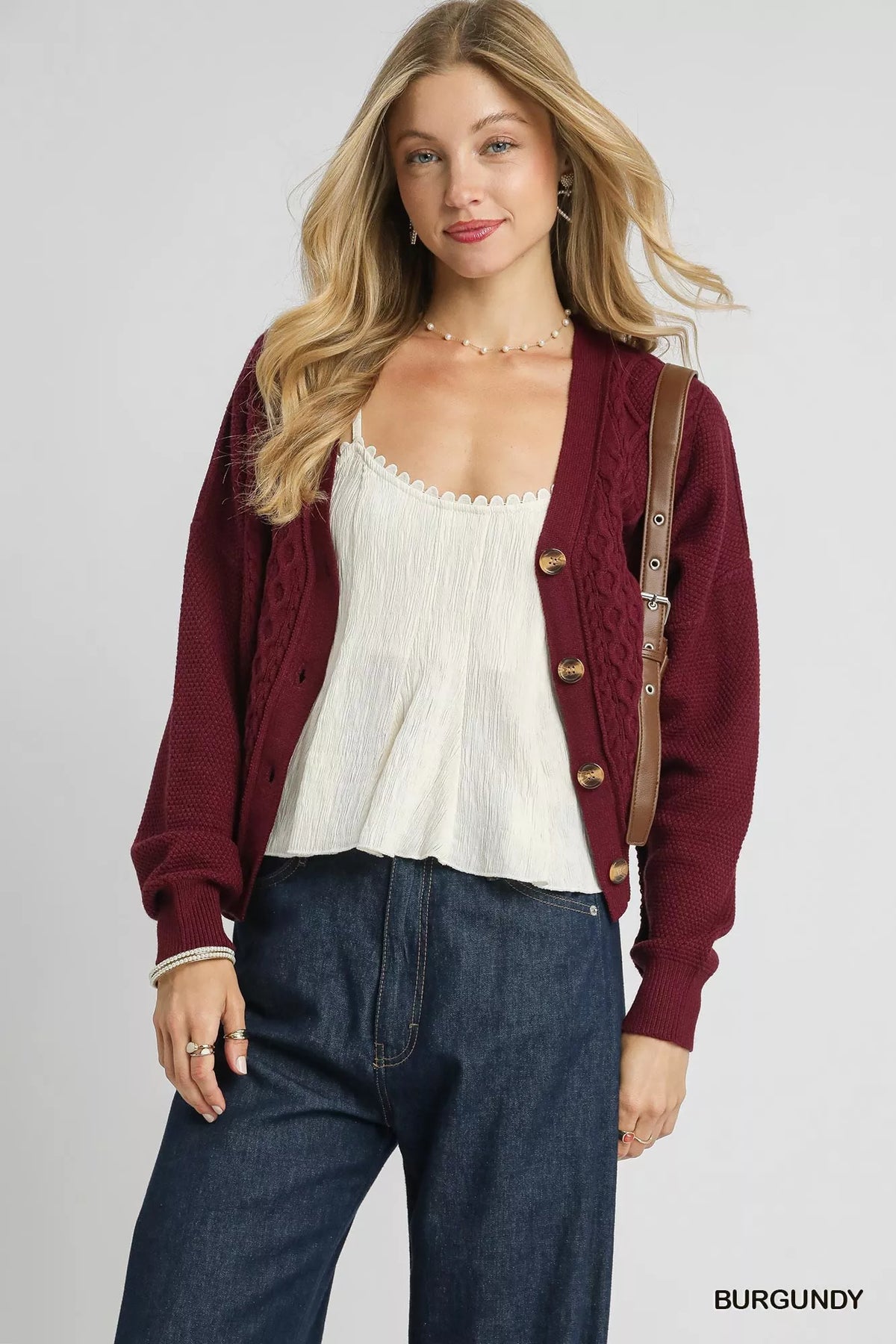 Woman wearing a burgundy knit cardigan over a white top with blue jeans, casual outfit