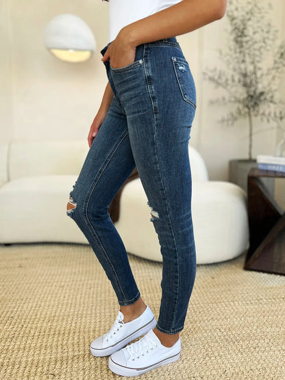 Woman wearing distressed blue skinny jeans and white sneakers in a modern living room