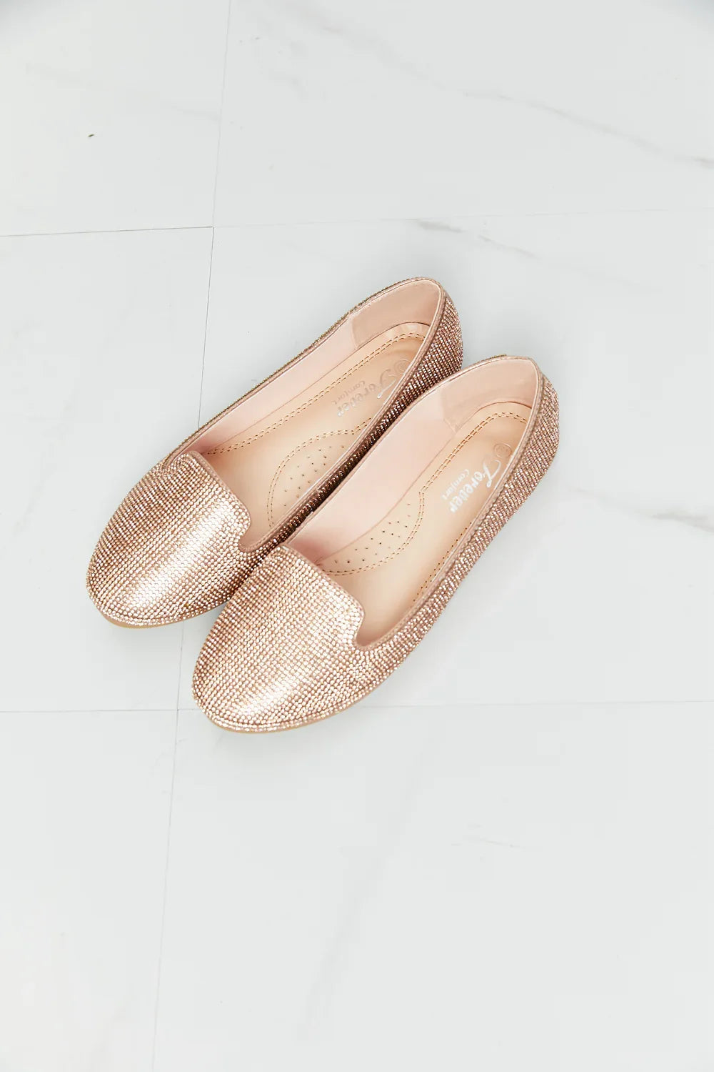 Pair of rose gold textured loafers with a pointed toe on a white tile floor