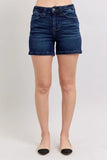 High-rise dark wash denim shorts with front button closure, modeled in a studio setting.