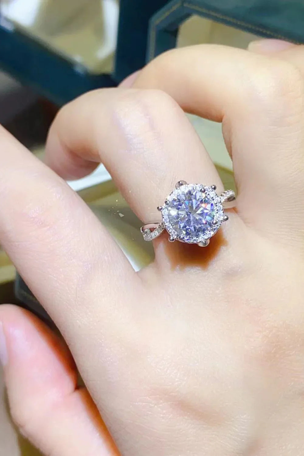 Close-up of a hand wearing a silver ring with a large round-cut gemstone and halo setting