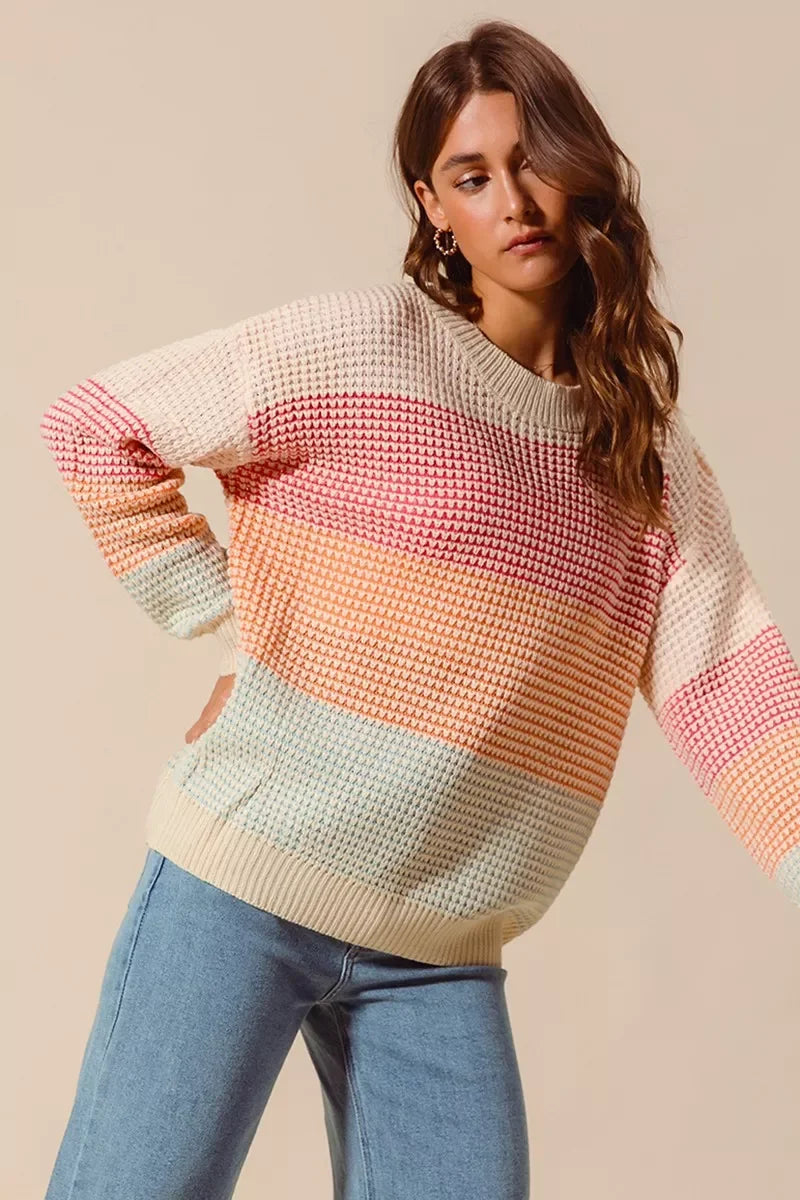 Woman wearing a pastel color block knit sweater with relaxed fit and light wash jeans