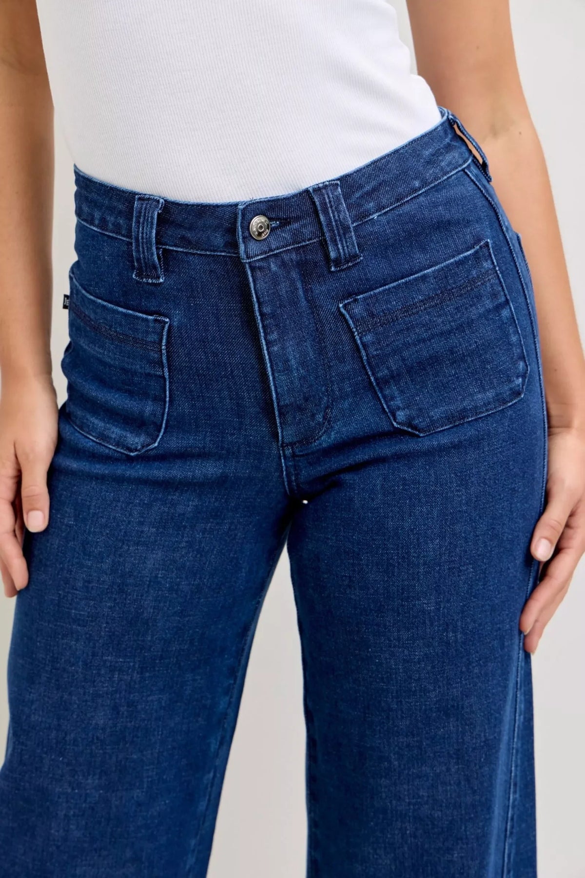 High-waisted wide leg blue denim jeans with front patch pockets, styled with white top.
