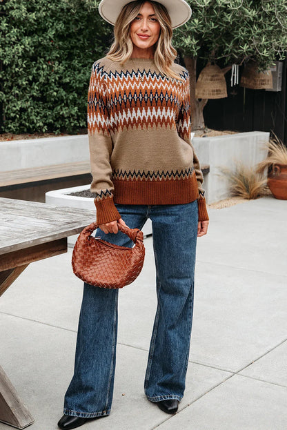 Woman in geometric patterned sweater, wide-leg jeans, and hat, holding a woven brown handbag outdoors.