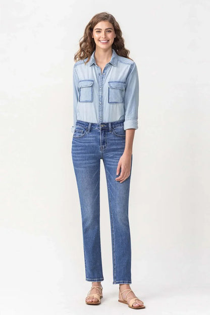 Woman wearing light chambray shirt and straight-leg blue jeans, standing on white background