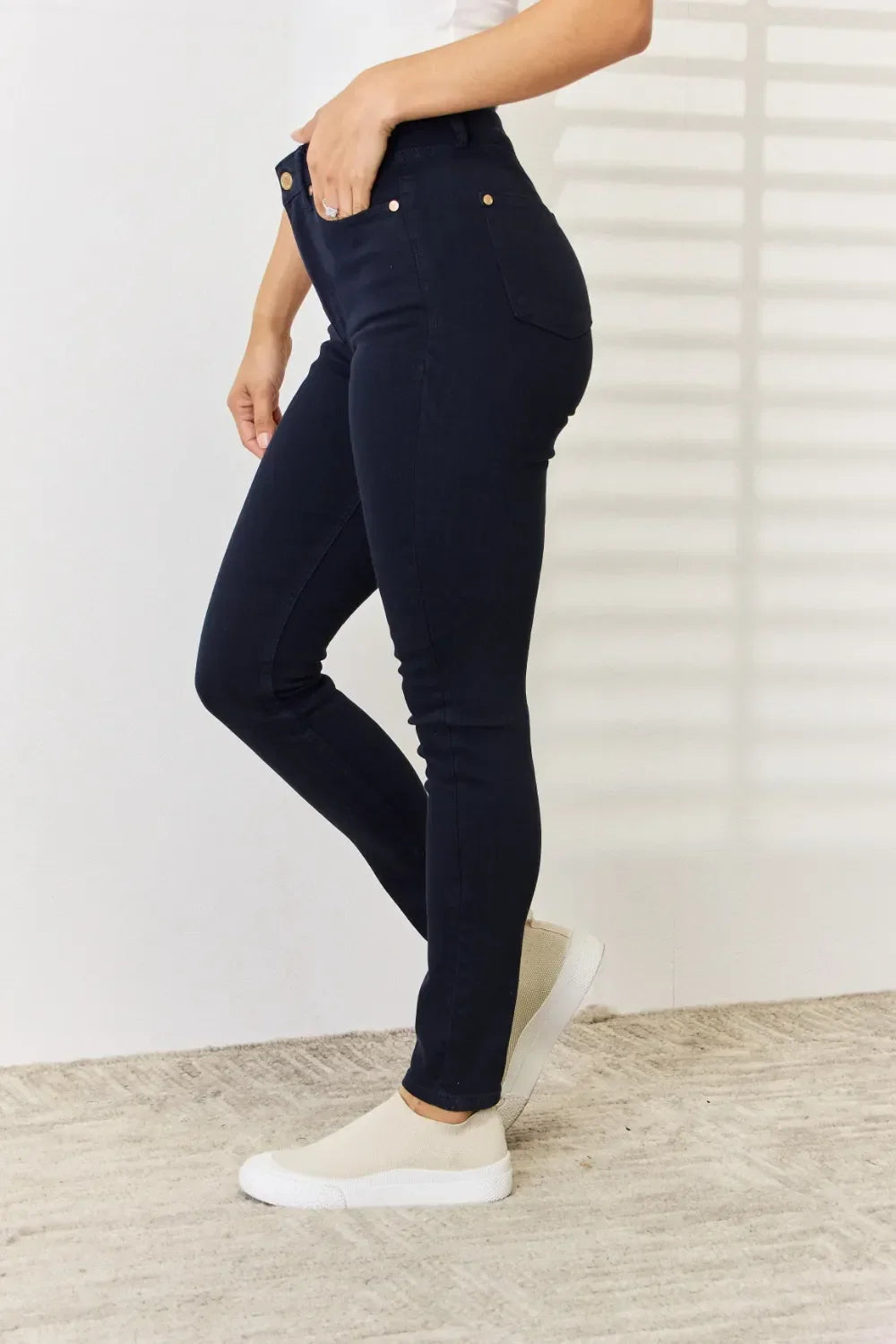 Woman wearing dark skinny jeans and cream slip-on sneakers, standing on a textured rug