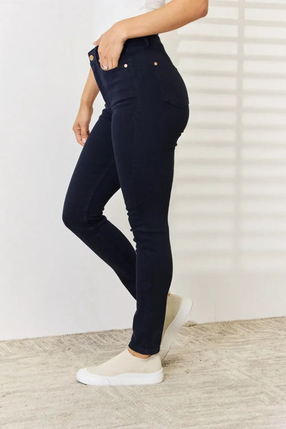 Woman wearing dark skinny jeans and cream slip-on sneakers, standing on a textured rug