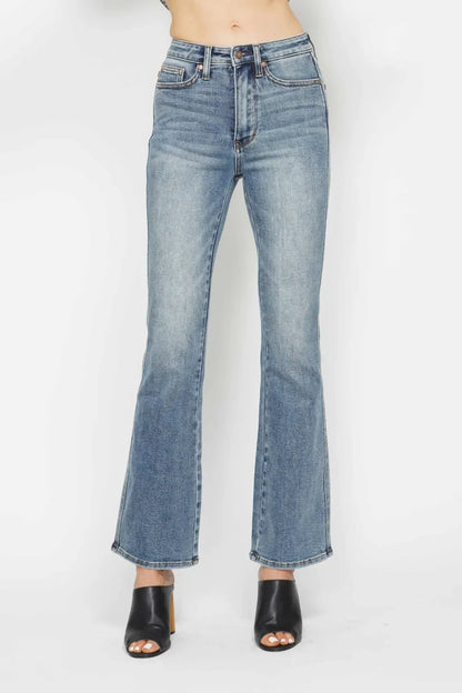 High-waisted distressed flare jeans styled with black heeled mules on white background