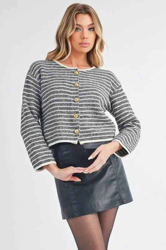 Woman wearing striped button-up cardigan and black faux leather mini skirt, standing indoors.