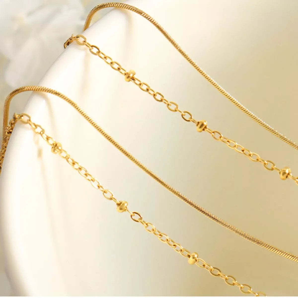 Minimalist gold layered chain necklaces with delicate links and bead accents on a neutral background